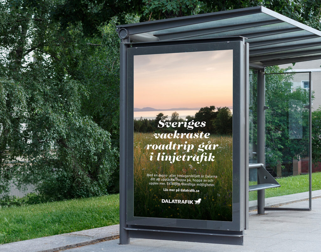 En busskur med poster på sidan med en vacker vy över siljan och en äng i solnedgången.
